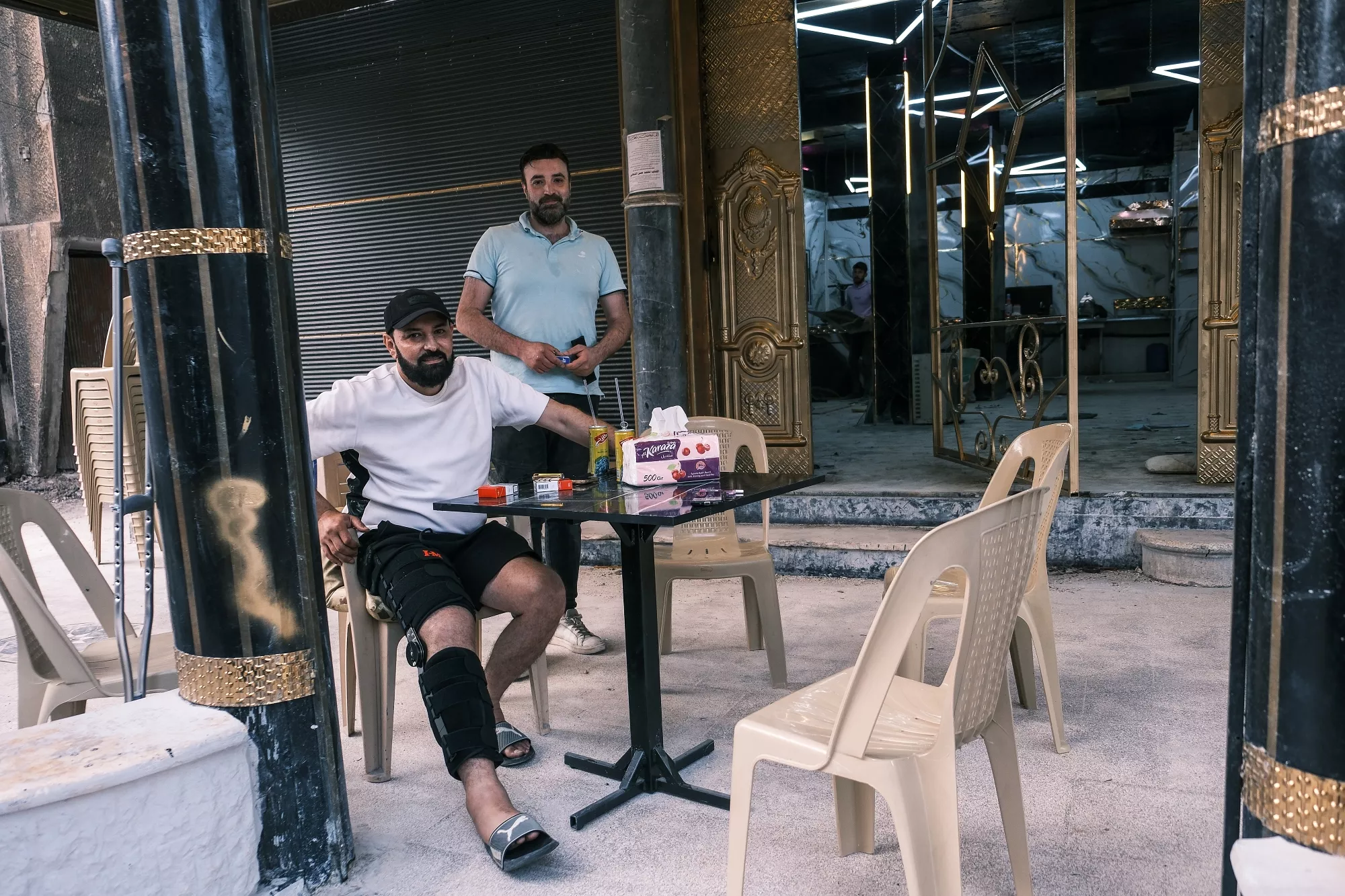 Due uomini in un bar, uno seduto con una stecca, e l'altro in piedi dietro di lui.