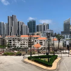 صورة لمدينة حديثة، مباني مرتفعة، سماء زرقاء وأشجار. يبدو النشاط العمراني واضحًا.