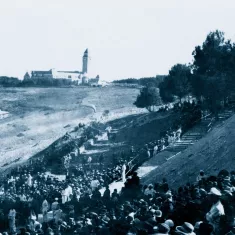 Un grande raduno di persone all'aperto, con un edifico distante e alberi circostanti.