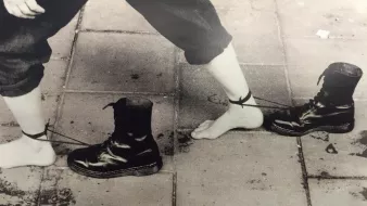 Des pieds nus liés à des bottes noires par des cordes. Image en noir et blanc.