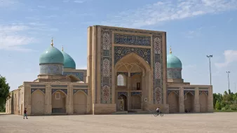 تظهر الصورة معمارًا تاريخيًا بأقواس وقباب زرقاء في سماء صافية. جو مريح.