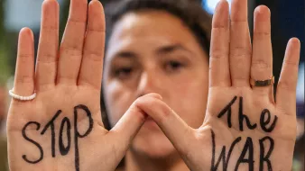 Une personne montre ses mains avec "STOP" et "THE WAR" écrits sur chaque paume.