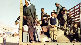 Gruppo di persone, molte famiglie e bambini, su un camion in un contesto di crisi.
