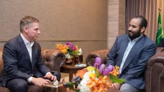 Deux hommes en costume assis dans un salon, entourés de fleurs colorées.