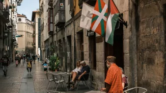 Vicolo affollato con tavolini all'aperto e bandiere che sventolano.