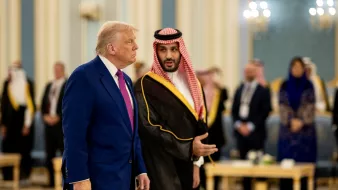 دو مرد در لباسهای رسمی مختلف در یک محیط مجلل با نور ملایم و حضور افرادی دیگر.