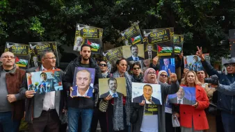 L'image montre un groupe de personnes réunies lors d'une manifestation. Elles tiennent des pancartes et des portraits de personnalités, exprimant des messages de soutien. L'ambiance est dynamique, avec des visages souriants et engagés.