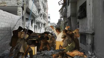 L'image montre une scène tragique dans une rue ruineuse. On peut y voir des bâtiments endommagés, des débris sur le sol et une atmosphère de chaos. Au centre, des personnages semblent exprimés des émotions intenses, avec des gestes qui suggèrent désespoir et lutte. La juxtaposition des figures humaines avec l'environnement détruit souligne la gravité de la situation. L'éclairage met en avant le contraste entre les ombres et les zones éclairées, créant une ambiance dramatique.