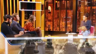 Quatre personnes discutent sur un plateau, avec une vue citadine illuminée en arrière-plan.