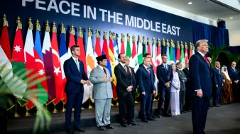 A group of leaders stands in front of flags, with one man speaking, promoting Middle East peace.