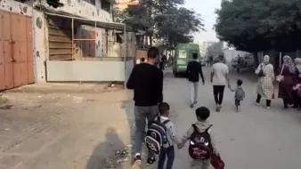 Un uomo cammina con due bambini, mentre altre persone si muovono in una strada cittadina.