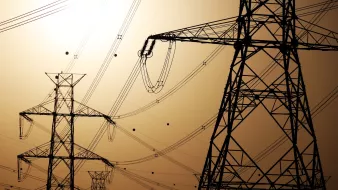 Silhouettes de pylônes électriques contre un ciel orangé.