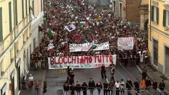 Una grande manifestazione con moltissime persone che sfilano, portando striscioni.