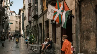 Ruelle animée avec tables de café, drapeaux et passants au style basque.