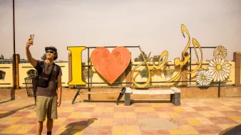 Un homme prend un selfie devant une grande inscription colorée "I ❤️ [nom]".