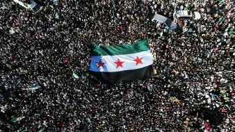 Une foule dense brandit un grand drapeau noir, blanc et vert avec trois étoiles rouges.