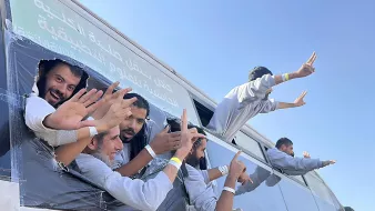 Gruppo di persone sorridenti sporge da un bus con le mani alzate, in un'atmosfera festosa.
