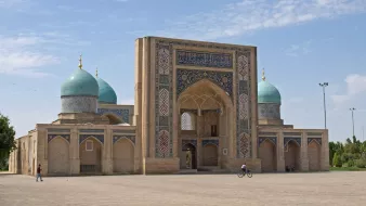 Bâtiment en brique avec de grandes arches et coupoles turquoise sous un ciel bleu.