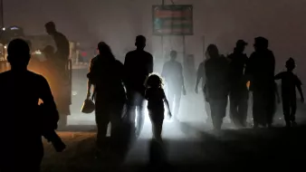 Silhouettes of people walk through fog; a child stands out in the light, creating a striking contrast.