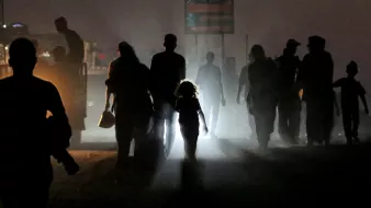 Una fila di persone in silhouette, una bambina con una luce al centro, in un'atmosfera misteriosa.