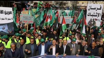 A large crowd marches, holding Palestinian flags and banners, in a show of solidarity.