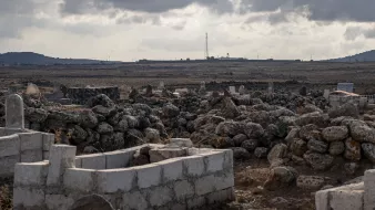 Un paisaje árido con tumbas y rocas, bajo un cielo nublado y distante, se ve una torre.