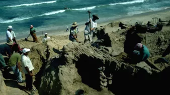 Des archéologues creusent sur une plage, entourés de sable et de vagues.