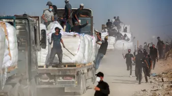 Des camions chargés de marchandises, des travailleurs en mouvement dans la poussière.