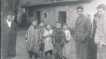 Groupe d'enfants en tenue traditionnelle, devant une maison, ambiance d'époque.