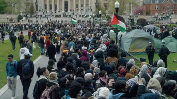 Un grand rassemblement de manifestants avec des drapeaux, dans un parc.