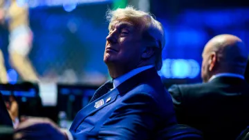 Homme en costume bleu, assis, regarde un événement sportif en direct.