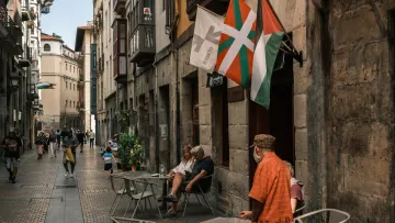 Vicolo affollato con tavolini all'aperto e bandiere che sventolano.