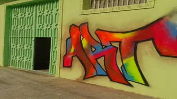 L'image montre un mur coloré peint en graffiti, où le mot "ART" est mis en avant. Les lettres sont stylisées avec des couleurs vives, notamment du rouge, du jaune, du orange et du bleu, se détachant sur un fond de mur vert. À côté du graffiti, on aperçoit une porte ouverte, ajoutant du caractère à l'ensemble de la scène. Le style du graffiti donne une impression dynamique et artistique à cet espace.