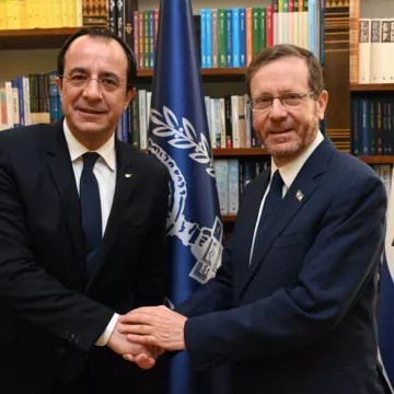 Deux hommes en costume se serrent la main devant des drapeaux et des étagères de livres.