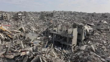 L'image montre un vaste paysage de débris et de bâtiments effondrés, engloutis dans les gravats. On aperçoit des structures en béton brisées et une atmosphère de destruction désolante.