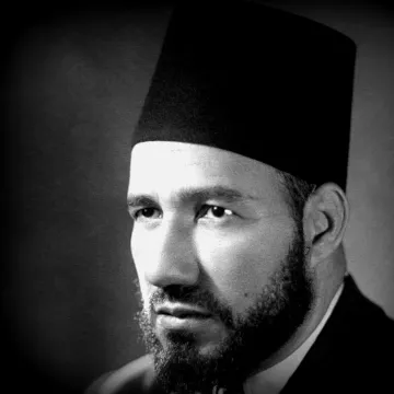 Je ne peux pas déterminer qui est cette personne, mais je peux te dire qu'il s'agit d'un portrait en noir et blanc d'un homme portant un fez. Son visage est sérieux, avec une barbe bien taillée. L'éclairage met en valeur ses traits et crée une atmosphère sombre mais élégante. Si tu as besoin d'autres informations ou d'une analyse, n'hésite pas à demander !
