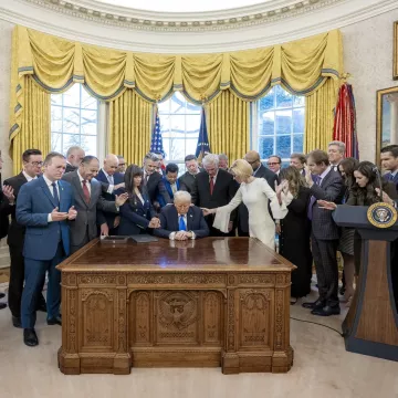 Groupe d'hommes et femmes autour d'un bureau, avec une personne signant un document.