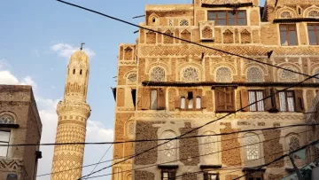 Vieilles maisons en briques, motifs géométriques, minaret élancé sous un ciel bleu.