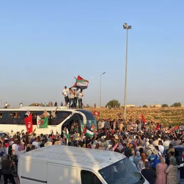 Une foule rassemblée autour d'un bus, brandissant des drapeaux et des pancartes.