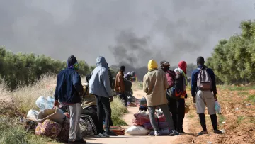 Un groupe de personnes se tient sur un chemin, entouré de fumée et de bagages.
