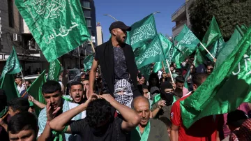 L'immagine mostra un gruppo di persone in una manifestazione. Molti partecipanti brandiscono bandiere verdi, che possono simboleggiare un movimento politico o religioso. Alcuni individui sembrano esprimere forti emozioni, con sorrisi e grida, mentre uno di loro è in piedi sopra la folla, probabilmente cercando di guidare o incoraggiare i manifestanti. Lo sfondo presenta edifici e un cielo sereno, suggerendo che l'evento si svolge all'aperto in una città.