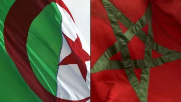 L'image montre deux drapeaux nationaux côte à côte. À gauche, le drapeau algérien, qui se compose d'une bande verte et blanche avec une étoile rouge et un croissant rouge. À droite, le drapeau marocain, qui est rouge avec un pentacle vert au centre. Les drapeaux flottent, créant une impression de mouvement et vibrant avec leurs couleurs.