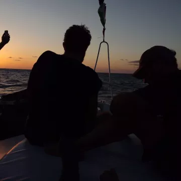 Silhouettes de personnes sur un bateau au coucher du soleil, mer calme.