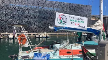 Una barca in un porto con un banner che supporta Gaza e un fondale moderno.