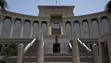 L'image montre un bâtiment imposant, probablement une institution judiciaire, avec une architecture moderne. La façade est ornée de colonnes majestueuses et de grandes fenêtres réfléchissantes, créant une impression de grandeur. Il y a des escaliers menant à l'entrée principale, qui semble être encadrée par des éléments décoratifs. Le ciel est dégagé, suggérant une journée ensoleillée. Des palmiers sont visibles sur les côtés, ajoutant une touche tropicale à l'environnement.