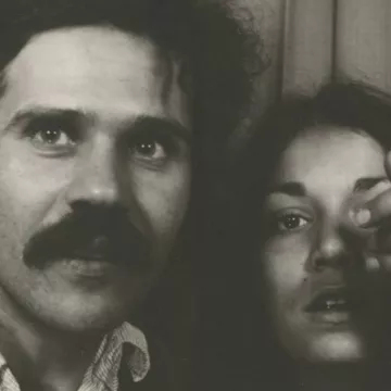 Un homme avec une moustache et une femme montrant un doigt vers l'objectif.