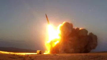 L'image montre le lancement d'un missile. On peut voir une grande flamme et une traînée de fumée qui s'échappent du sol alors que le missile s'élève dans le ciel. L'environnement semble désertique, avec un éclairage crépusculaire qui souligne la force de l'explosion et le mouvement ascendant du projectile.