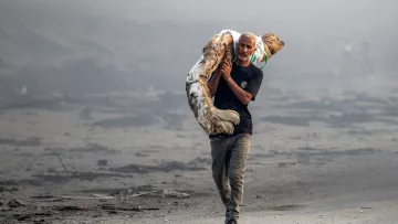 Un homme portant un corps dans un paysage dévasté et brumeux.