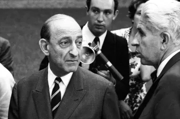 Deux hommes en costume, discutant sérieusement, entourés d'autres personnes. Époque rétro.