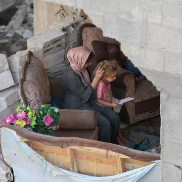 Une mère réconforte son enfant dans un espace endommagé, entourés de débris.